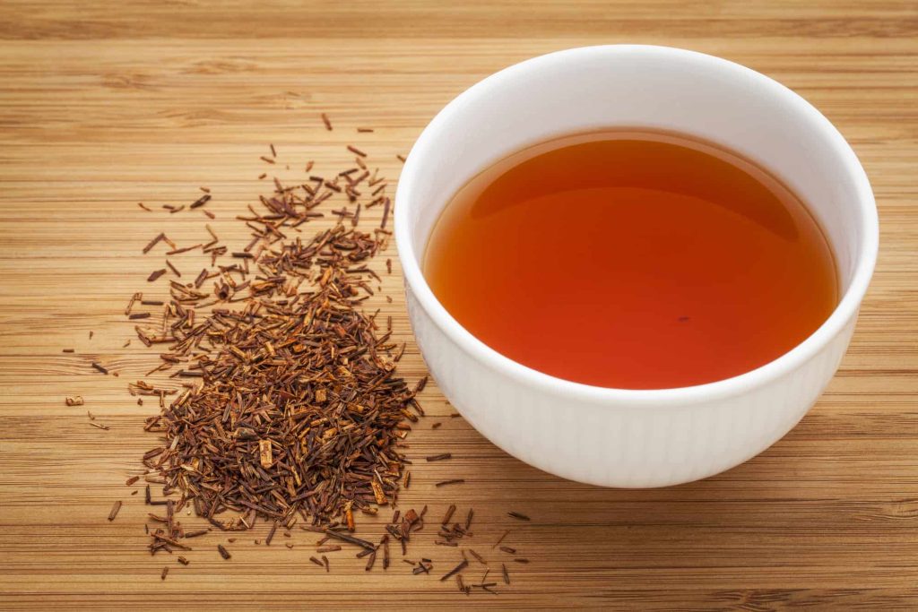 rooibos red tea in a white cup and loose leaves 