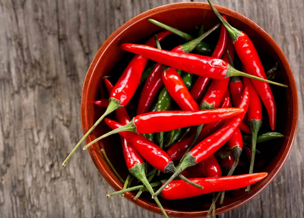 Fresh green chilli peppers, whole and sliced, on a dark surface