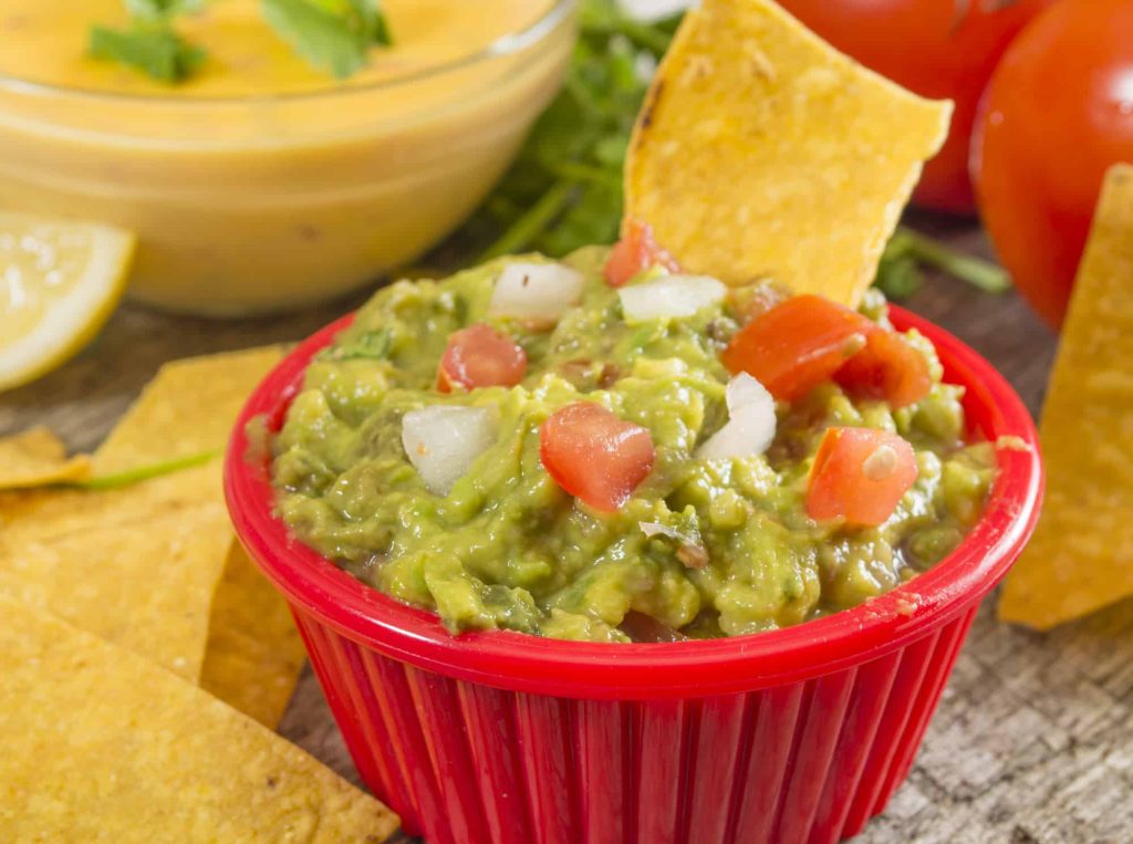 pico de gallo added to guacamole in a bowl