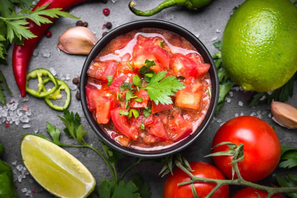 watery pico de gallo in a bowl and ingredients on a table