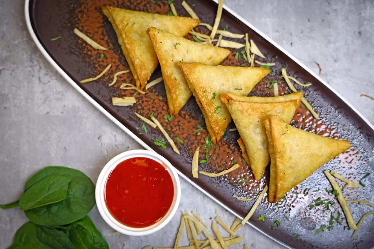 Samosas fried golden, one broken open to show the spiced potato and pea filling.