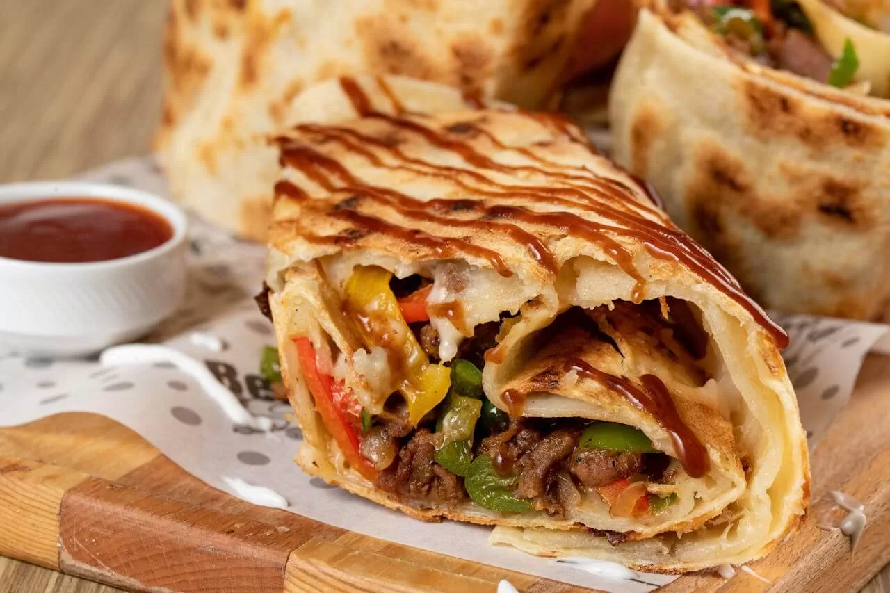 Burritos wrapped in large flour tortillas, one cut open to show rice, beans, meat and cheese inside.