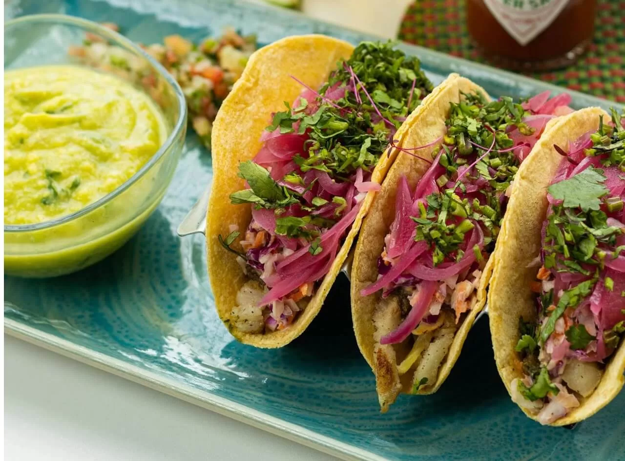 Classic chicken tacos on soft corn tortillas, topped with diced onion, coriander and a wedge of lime.