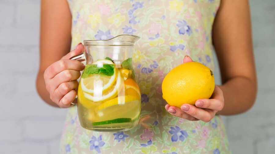 A woman holds a pitcher of water infused with fresh lemons, inspired by Beyoncé's lemonade diet. The vibrant colors suggest refreshment.