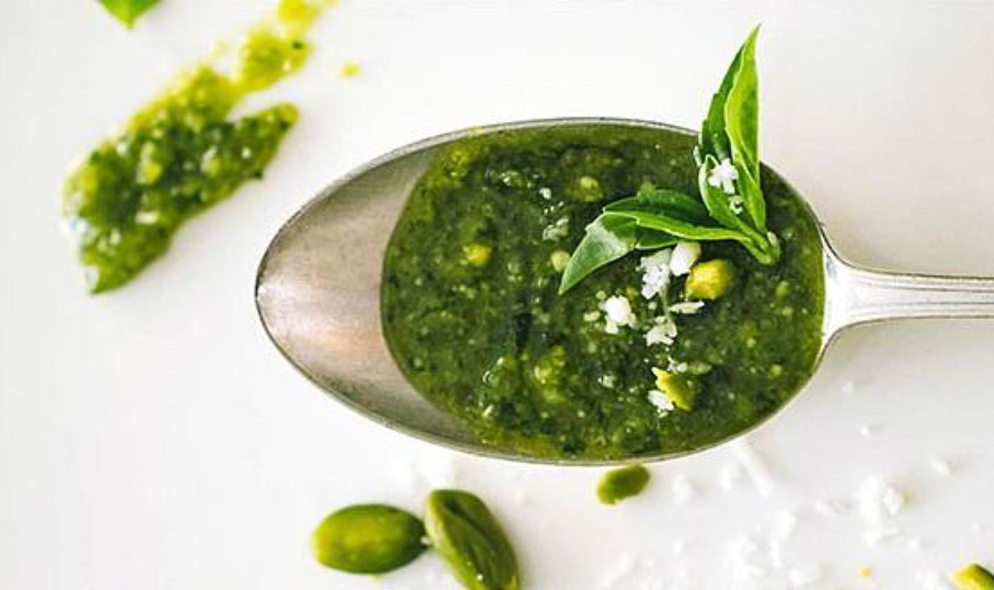 Green herb pesto in a spoon with fresh basil leaves