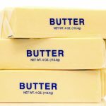Three sticks of butter stacked on top of each other against a white background. Each stick is labeled "BUTTER, NET WT. 4 OZ (113.4 g)" in blue text, revealing how much water content may vary by stick.