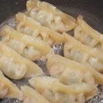 Eight dumplings sizzle in a black skillet, with oil bubbling around them, showcasing a light golden-brown edge. Whether you savor them hot or eat cold, these dumplings promise mouthwatering delight.