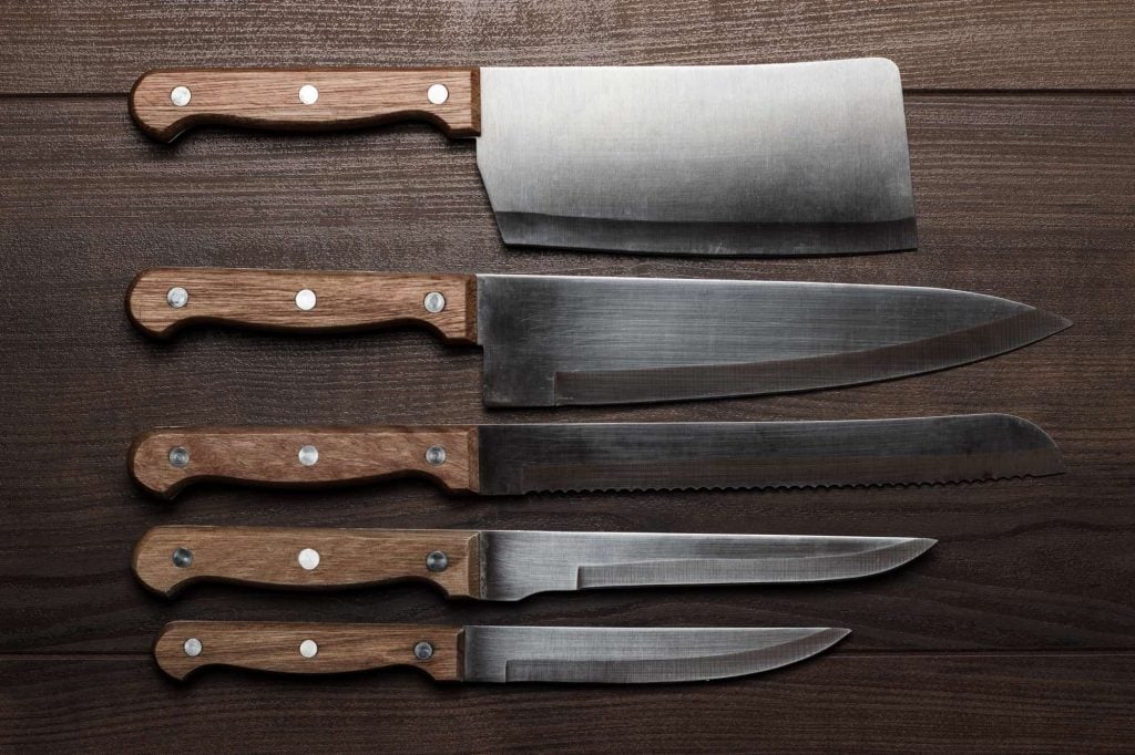 five kitchen knives on a brown table