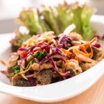 A vibrant dish featuring crispy fried salmon skin topped with a colorful mix of shredded cabbage, carrots, and red onions. Garnished with fresh lettuce leaves, it's presented on a white plate set on a wooden surface.