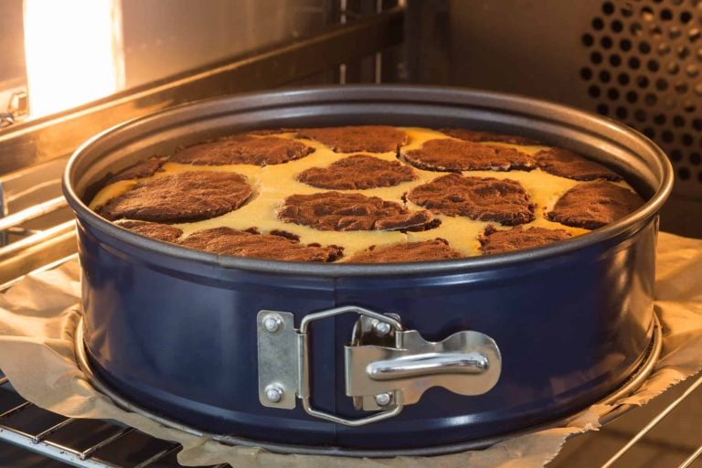 A chocolate marble cake bakes in a blue cake pan inside the oven, its swirling pattern of chocolate and yellow batter illuminated by the oven light. While similar to a pie pan, the design highlights subtle differences suitable for perfect cake creation.