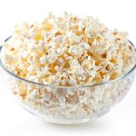 A clear glass bowl filled to the brim with fluffy, freshly popped popcorn, showcasing its light and airy texture on a clean white background – a delightful snack that’s perfect for those embracing a paleo lifestyle.