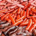 An assortment of sausages is displayed in three distinct rows, showcasing a variety of colors and textures, including reddish-brown, bright red, and deep brown hues—a true guide to the perfect paleo indulgence.