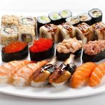 A variety of sushi dining options arranged on a white plate, featuring rolls with avocado, cucumber, and sauce, nigiri with shrimp, salmon, and eel, and gunkan adorned with fish roe and diced fillings. Perfect for those exploring delicate flavors while considering a Paleo diet.