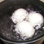Three hard boiled eggs gently simmer in a pot of water, with bubbles forming around them.