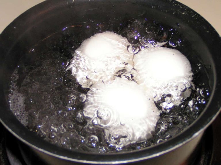 Three hard boiled eggs gently simmer in a pot of water, with bubbles forming around them.