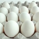 A close-up of a dozen white eggs arranged in a gray egg carton, evenly spaced in four rows of three. The background is a plain, bright surface, highlighting the smooth texture of the eggs, perfectly timed to catch their natural sheen.