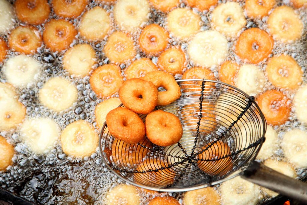 cooking medu vada in a pan using mesh ladle