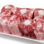 A white tray filled with raw oxtail pieces, displaying a mix of red meat and white bone sections. The oxtails are arranged closely together, showcasing their marbled texture and circular bone centers, perfect for cooking oxtails to perfection.