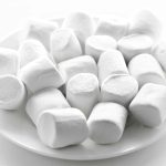 A white plate filled with a pile of fluffy vegan marshmallows. These cylindrical treats, perfect for any occasion, are set against a plain white background. Wondering where to buy your own batch? Look no further!