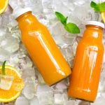 Two glass bottles of refreshing orange juice on ice, surrounded by vibrant orange slices and mint leaves. The white-capped bottles are artfully angled, creating a setting that captures the zest of freshly squeezed juice and the natural effervescence reminiscent of sparkling gas beverages.