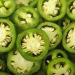 Close-up of sliced green jalapeños, highlighting their seeds and fresh texture. The vibrant layers invite you to eat, revealing not just flavor but also potential health effects. Circular slices are artfully layered to create a captivating textured pattern.