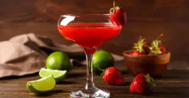 a glass of strawberry daiquiri with fresh strawberries and limes