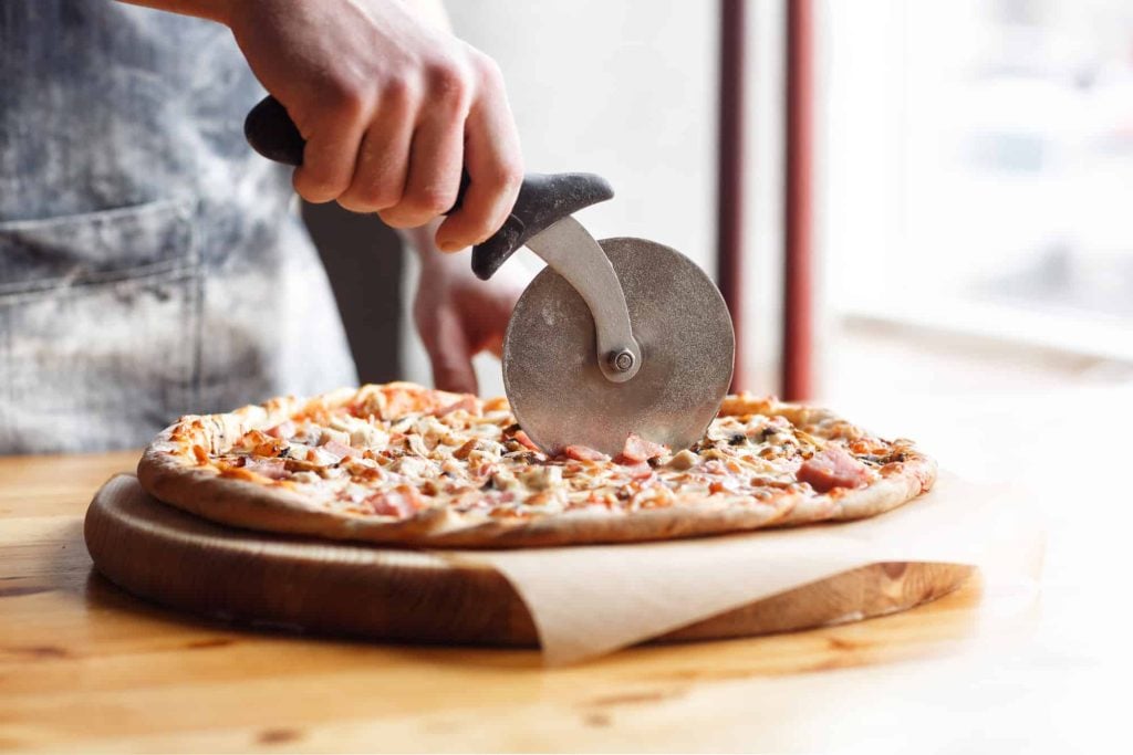 a person cutting a frozen pizza