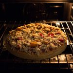 A pizza topped with cheese, bell peppers, and other toppings is baking perfectly in the oven. The oven light casts a warm glow, highlighting the melting cheese and vibrant colors of the toppings—a testament to masterful oven cooking.