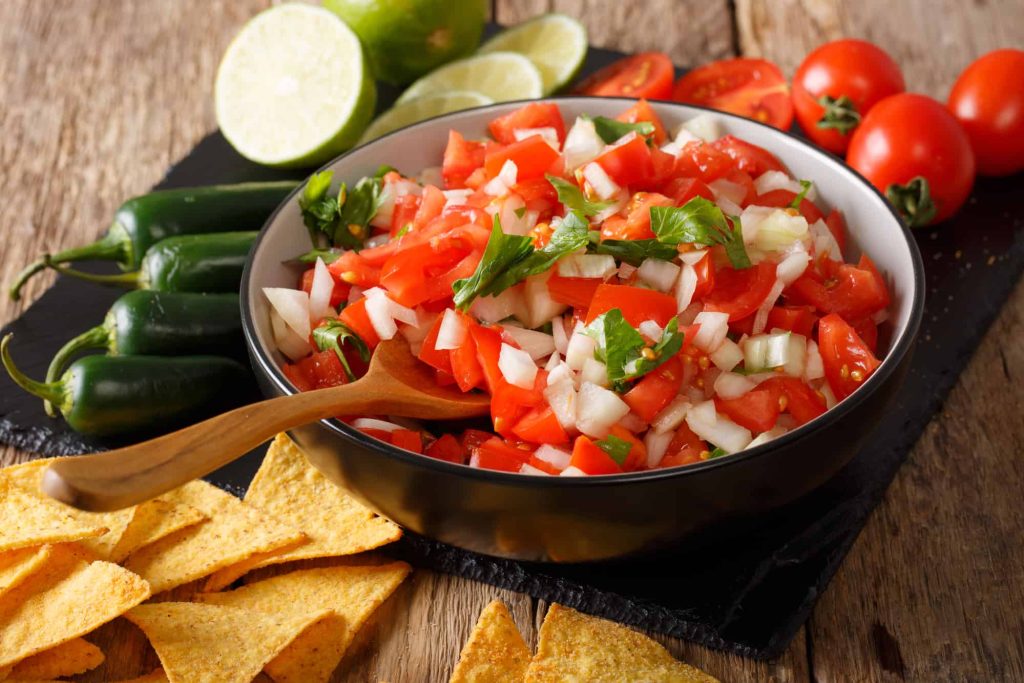 Mexican pico de gallo from tomatoes, onions, cilantro and jalapeno pepper in a bowl and nachos on a table. 