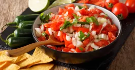 Mexican pico de gallo from tomatoes, onions, cilantro and jalapeno pepper in a bowl and nachos on a table.