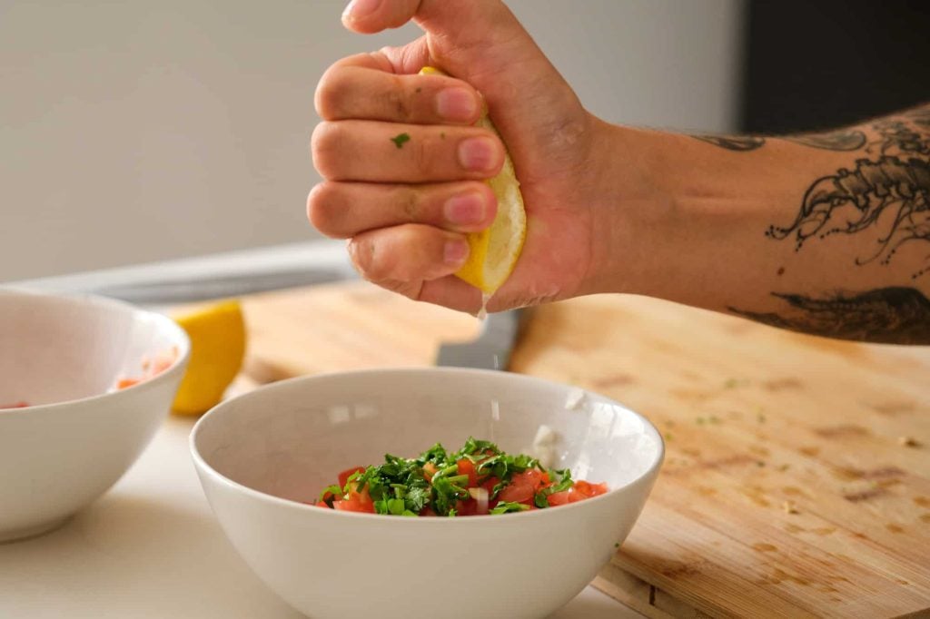 tattooed man adding lemon to the pico de gallo recipe