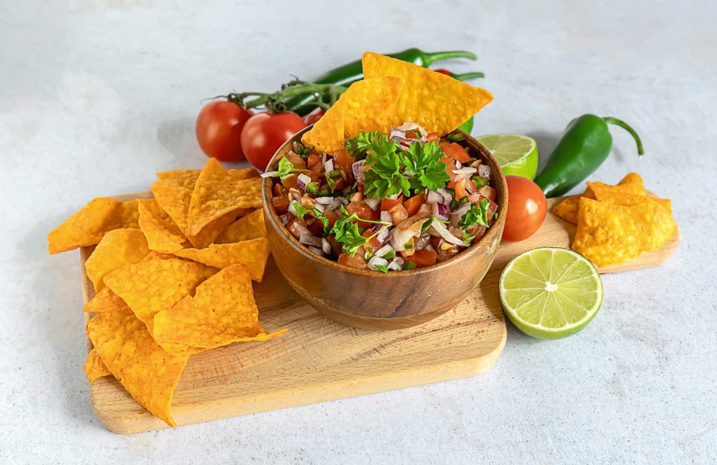 a bowl of pico de gallo with parsley and other ingredients on a cutting board