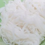 Close-up of white rice vermicelli noodles in a light green bowl. The noodles are tangled and shiny, highlighting their smooth texture and healthy appeal.