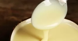 Bowl with condensed milk and spoon on table