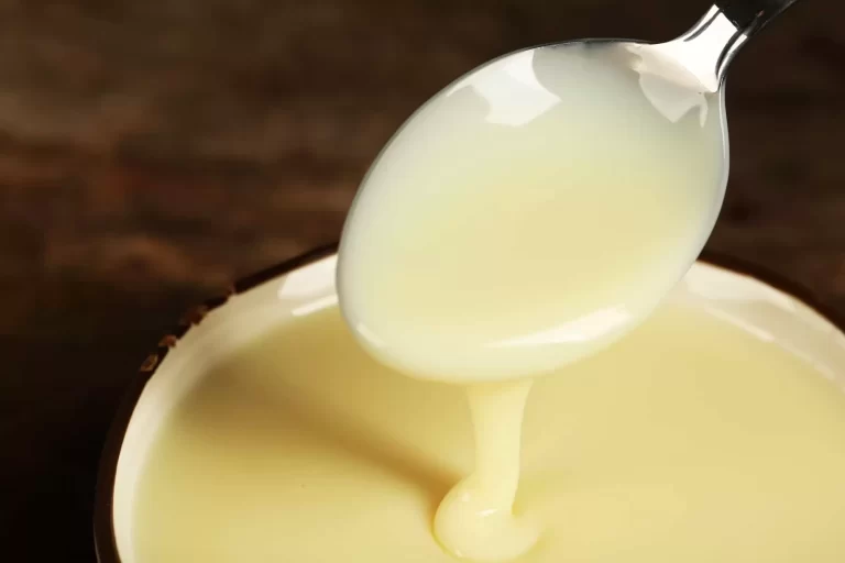 Bowl with condensed milk and spoon on table