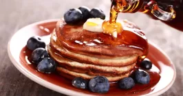 Pouring maple syrup on stack of pancakes