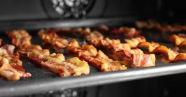 Baking tray with strips of bacon cooking in oven