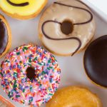 In a white box from Dunkin' Donuts, you'll find six delightful assorted donuts: a chocolate-glazed, a smiley face, a chocolate-drizzled, pink with sprinkles, dark chocolate, and plain glazed. A perfect treat for all patrons to enjoy.