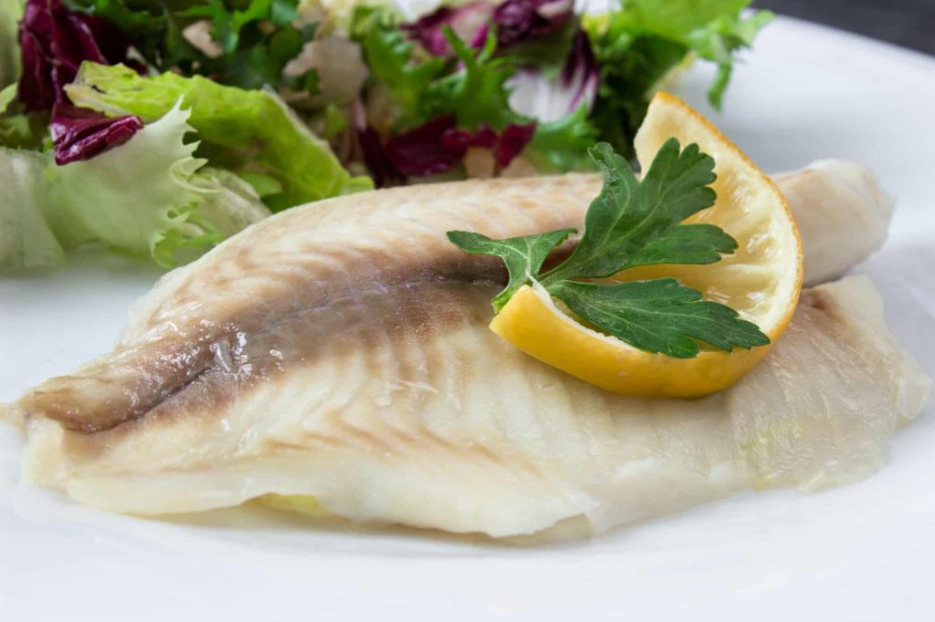 steamed tilapia fish with salad and slices of lemon