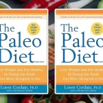 Two copies of "The Paleo Diet" book sit surrounded by fresh produce like avocados, tomatoes, nuts, and a lime, perfectly capturing the essence of the paleo diet's focus on natural foods.