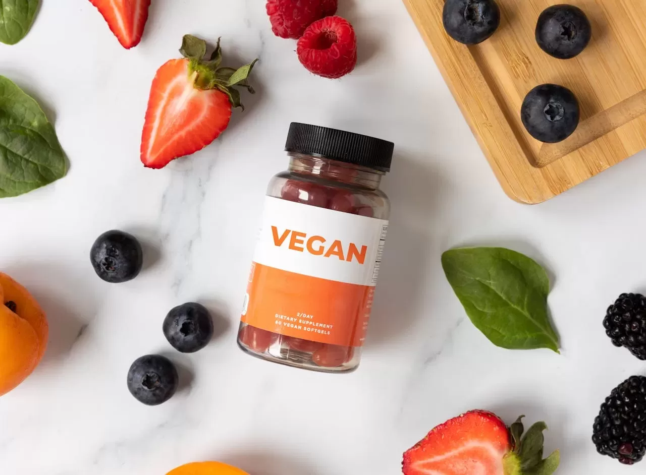 A "VEGAN" jar sits among fresh fruits and veggies—strawberries, blueberries, raspberries, spinach, and apricots—on a marble surface with a wooden cutting board peeking through. This vibrant scene invites you to discover key things to know about the vegan lifestyle.