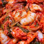 A close-up of freshly prepared kimchi, showcasing vibrant red chili paste coating Napa cabbage leaves, highlighting the rich texture and traditional fermentation process of this iconic Korean dish.
