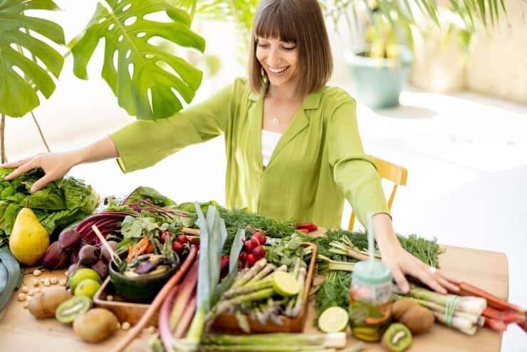 A woman stands in front of a table overflowing with fresh, colorful vegetables, ready for cooking or a healthy meal.