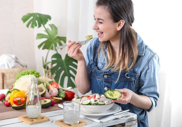 A woman enjoys a fresh salad, using a fork to savor each bite. The vibrant greens and colorful toppings are visible.