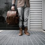 A man in a suit and brown shoes holds a stylish vegan leather bag, showcasing modern fashion and sustainability.