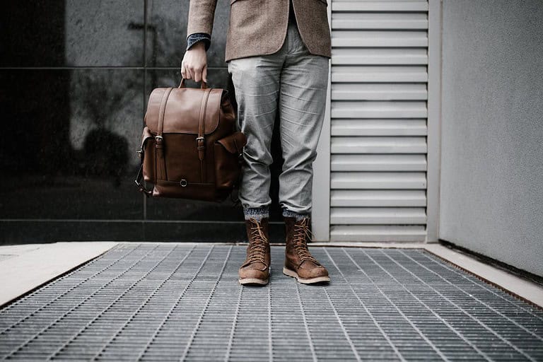 A man in a suit and brown shoes holds a stylish vegan leather bag, showcasing modern fashion and sustainability.