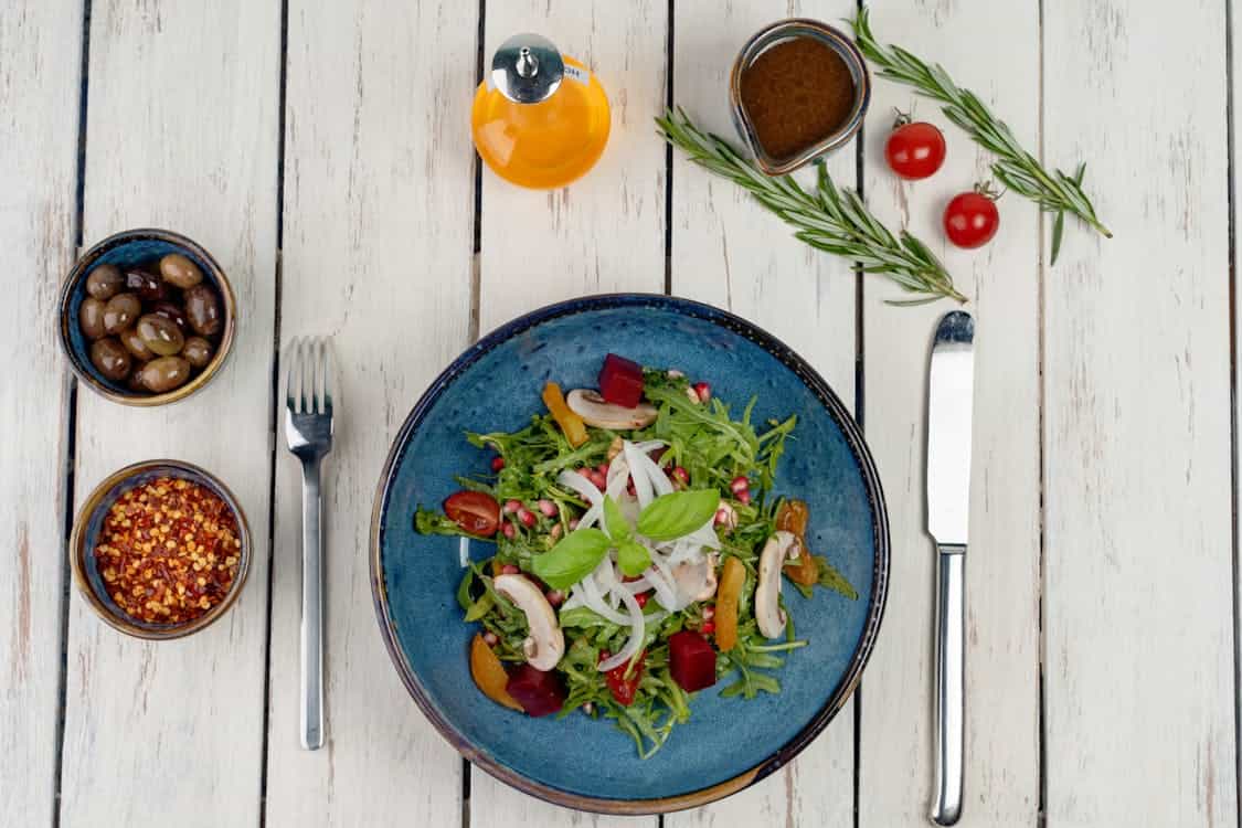 A blue plate holds a vibrant salad, accompanied by a knife and fork, promoting a vegan diet for digestive health.