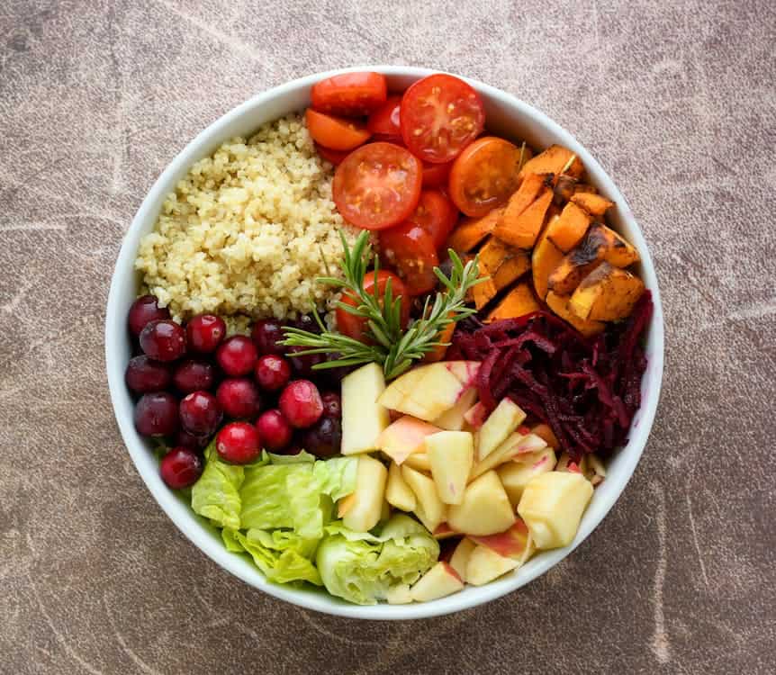 A vibrant bowl filled with fresh vegetables and fruits, accompanied by a side of quinoa, promoting a healthy vegan diet. 