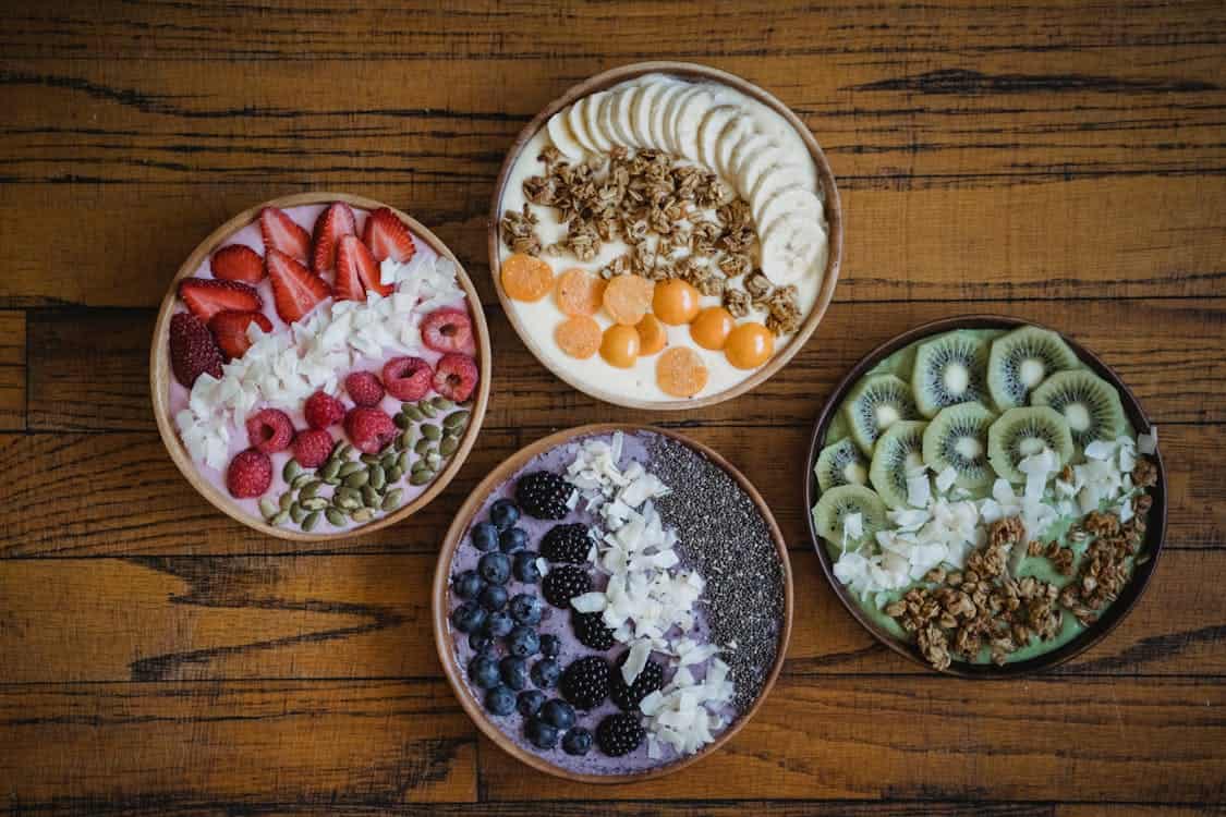 A wooden table displays four bowls filled with fresh fruit and yogurt, highlighting a vegan approach to a healthy digestive system.