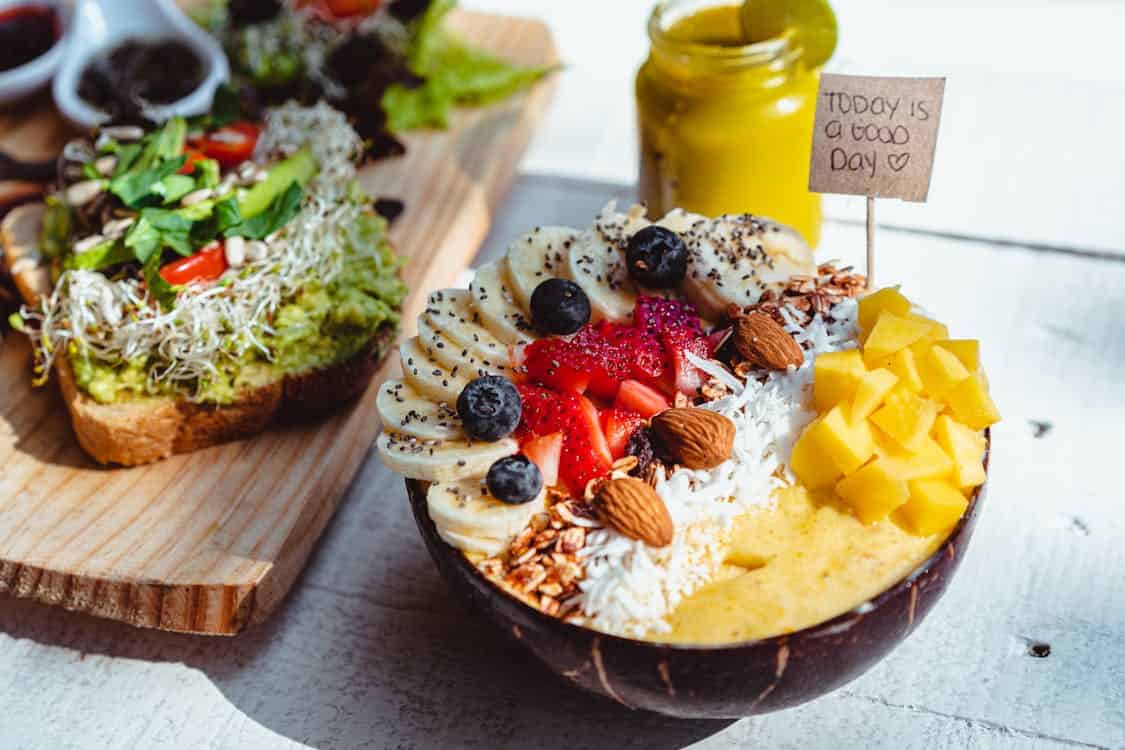  A bowl brimming with assorted fruits and vegetables, featuring a spoon positioned alongside the colorful display.